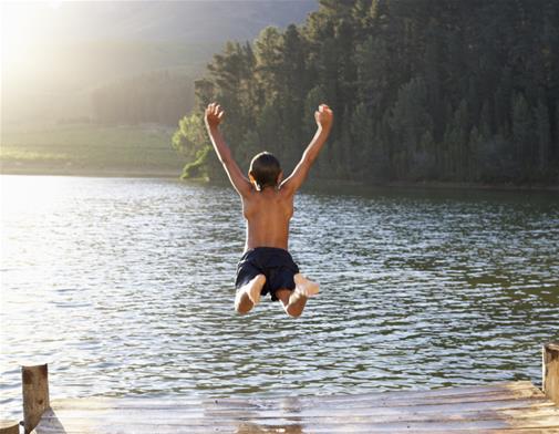 Barn som hoppar ner i en sjö från en brygga