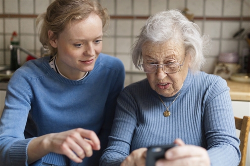 En äldre kvinna får hjälp med sin mobiltelefon.