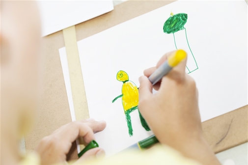 Hand som ritar en gubbe med tuschpennor i gult och grönt på vitt papper