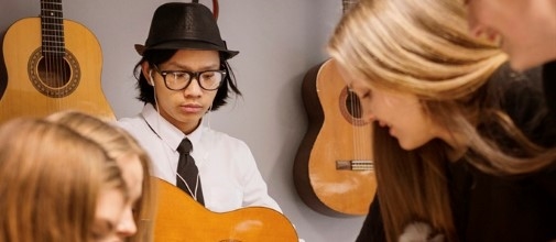 En ungdom spelar gitarr och andra ungdomar lyssnar.